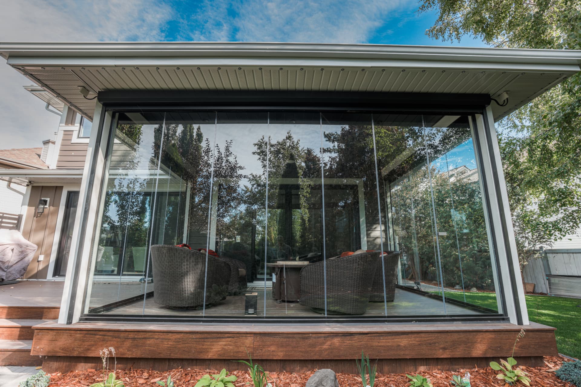Frameless glass patio enclosure on a wooden deck with wicker seating inside