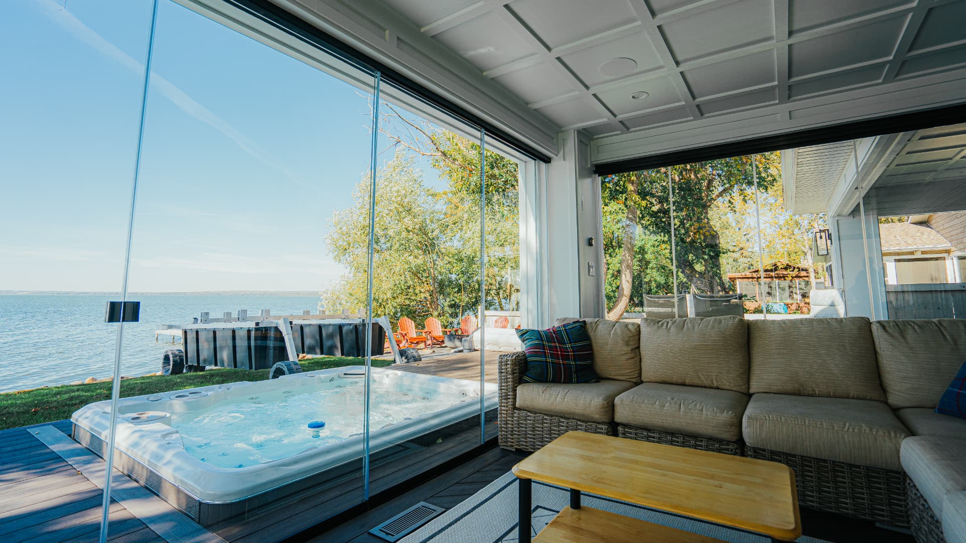 Retractable glass wall open beside a swim spa with a lake view