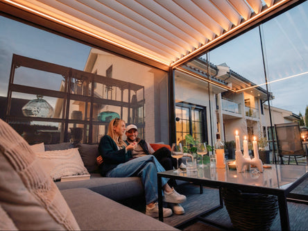 Louvered pergola with warm lighting over an outdoor lounge at dusk